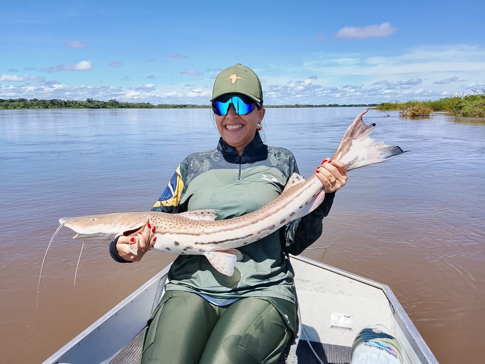 Pescadora num barco segura uma cachara pintada