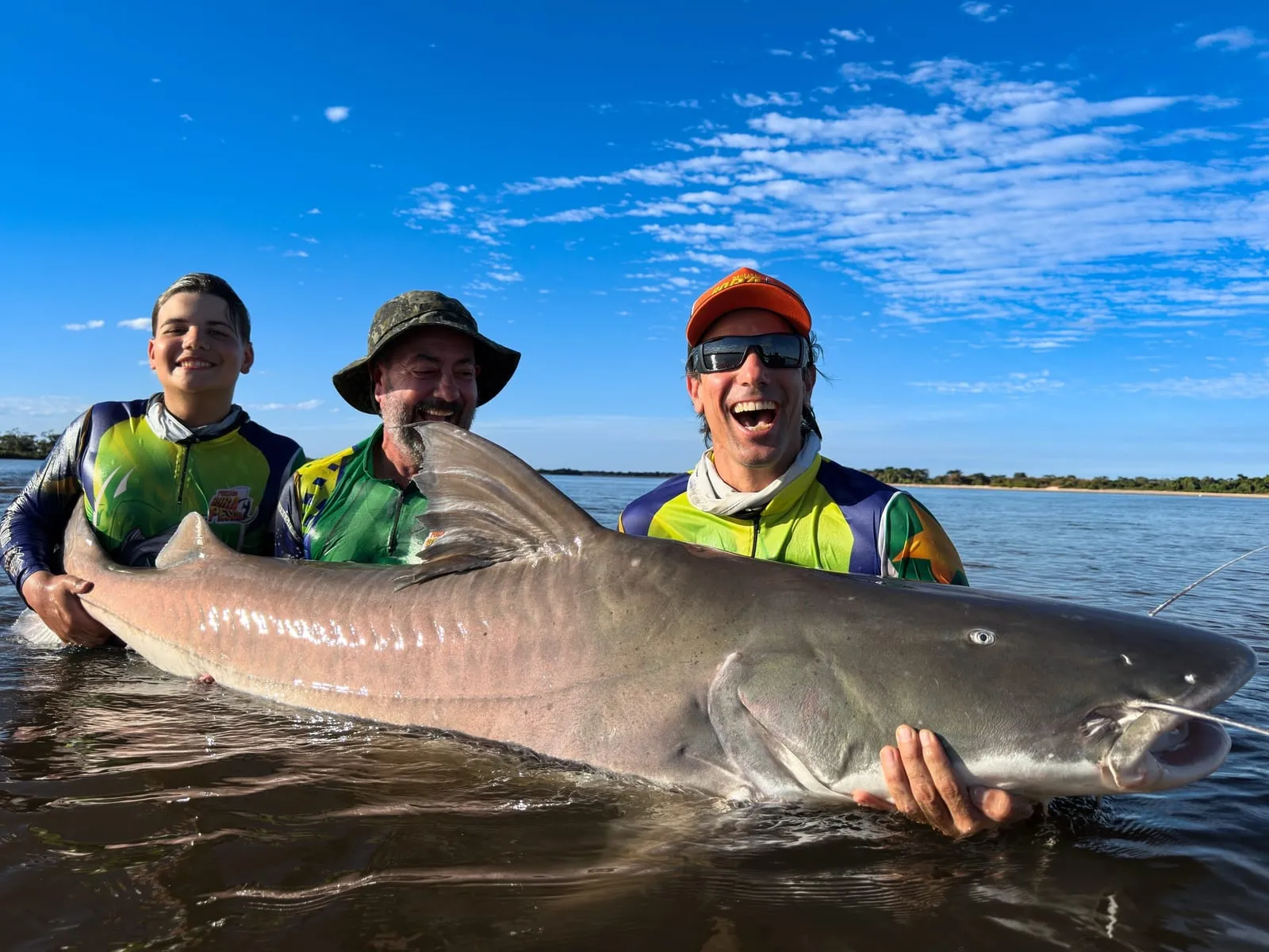 Três pescadores dentro do rio seguram uma piraíba enorme