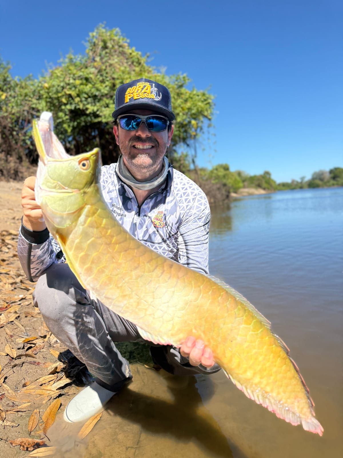 Pescador agachado na beira do rio segura uma aruanã