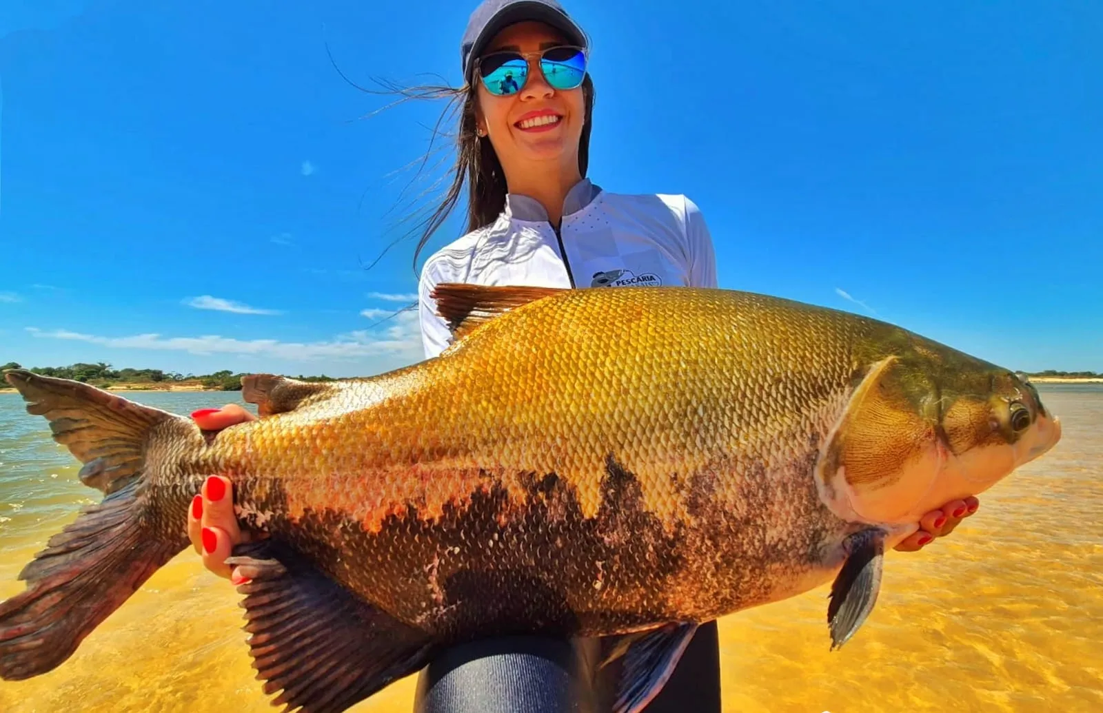 Pescadora segura um tambaqui na beira do rio