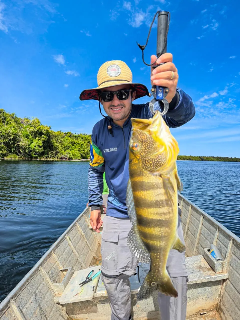 Pescador ergue um tucunaré preso no alicate