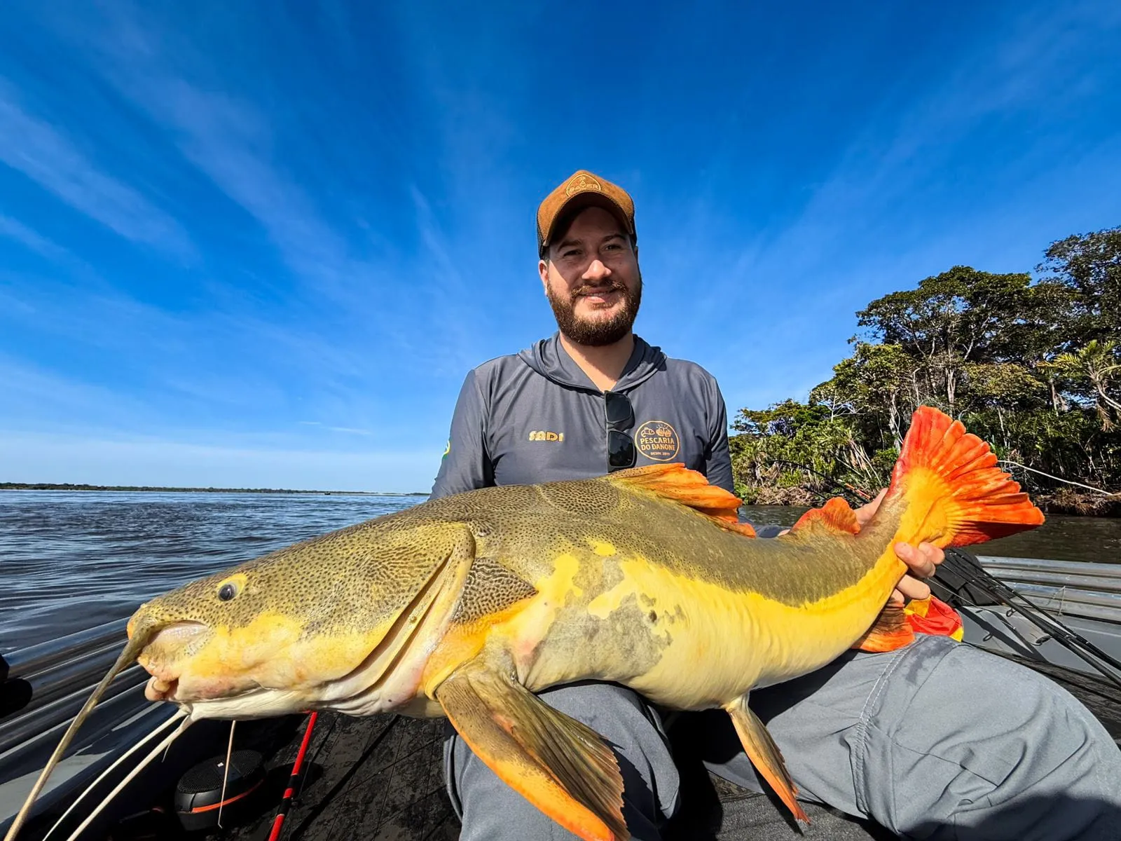 Pescador num barco segura uma pirarara de cauda vermelha