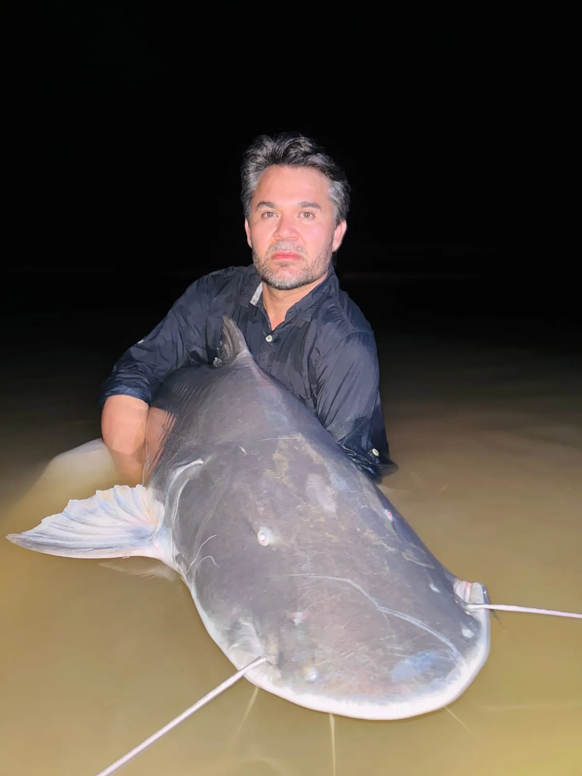 Pescador à noite segura uma piraíba na beira do rio