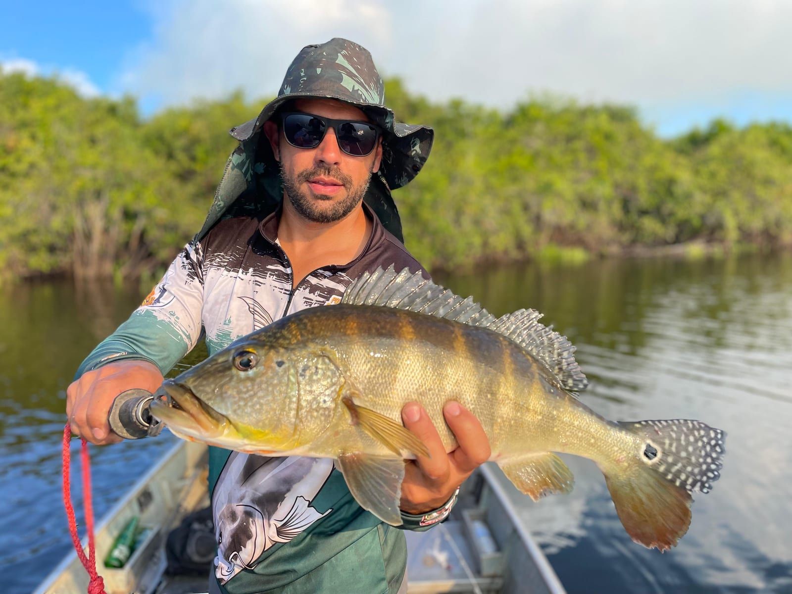 Pescador de chapéu segura um tucunaré