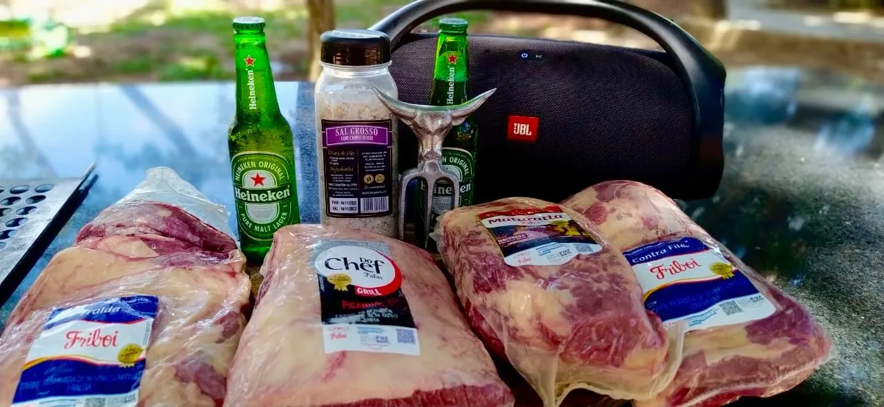 Peças de carne para o churrasco, com garrafas de cerveja ao fundo