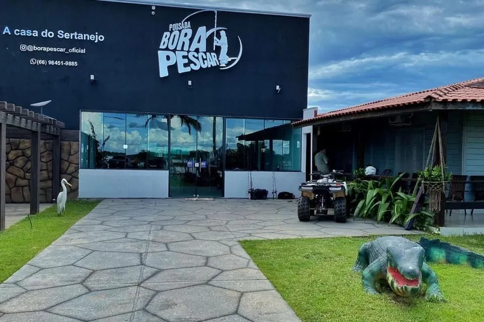 Fachada da Pousada Bora Pescar com caminho de pedra e escultura de jacaré no jardim
