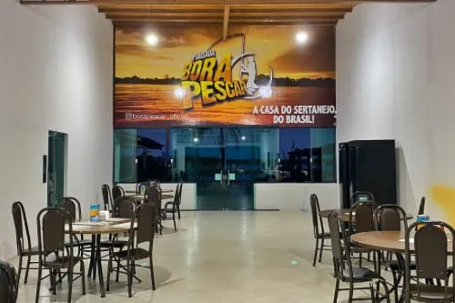 Salão com mesas redondas e painel da Bora Pescar ao fundo