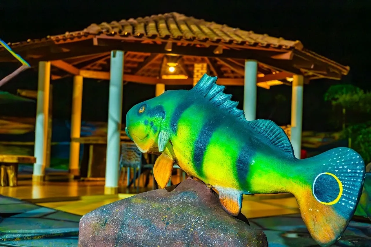 Escultura de tucunaré colorido diante de um quiosque iluminado à noite