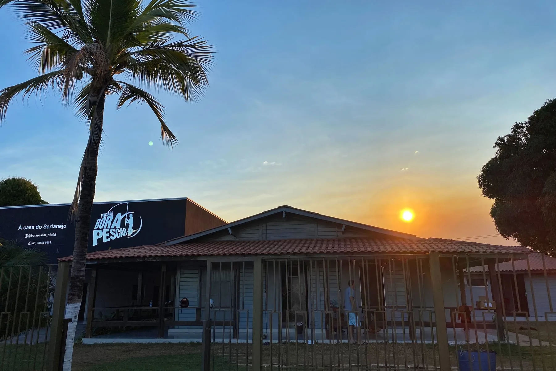 Prédio da pousada ao pôr do sol, com coqueiro na frente
