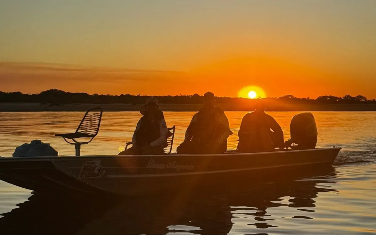 Três pescadores num barco no Rio Araguaia, em silhueta, ao pôr do sol