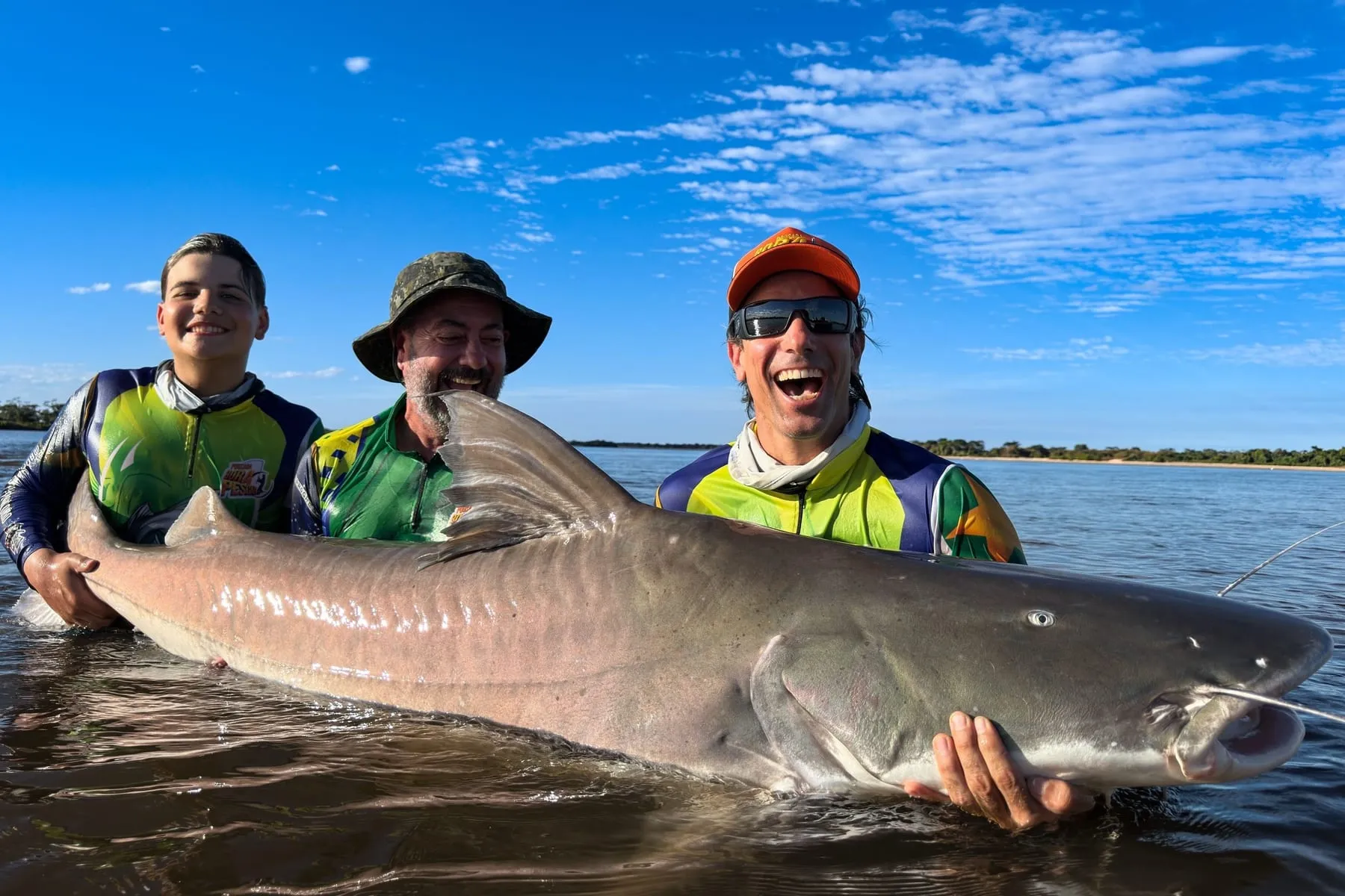 Três pescadores com um peixe de couro enorme na água