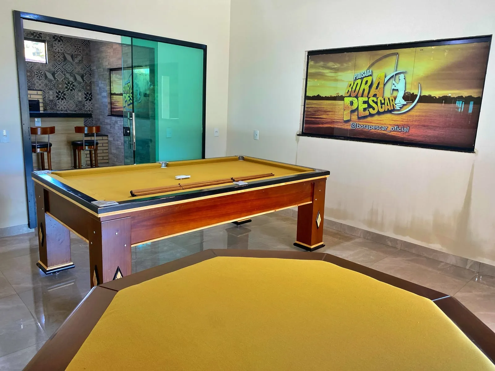 Mesa de sinuca no salão, com painel da Bora Pescar na parede